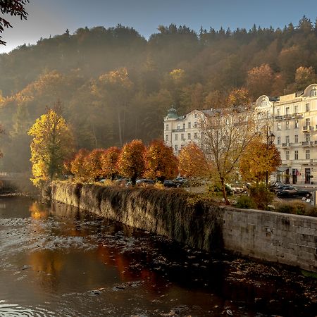 Grandhotel Pupp Κάρλοβι Βάρι Εξωτερικό φωτογραφία The photo depicts a serene riverside scene during autumn. The river flows gently, reflecting the warm hues of the trees along its banks. On one side, there are vibrant orange and yellow trees, showcasing the beautiful fall foliage, while the opposite