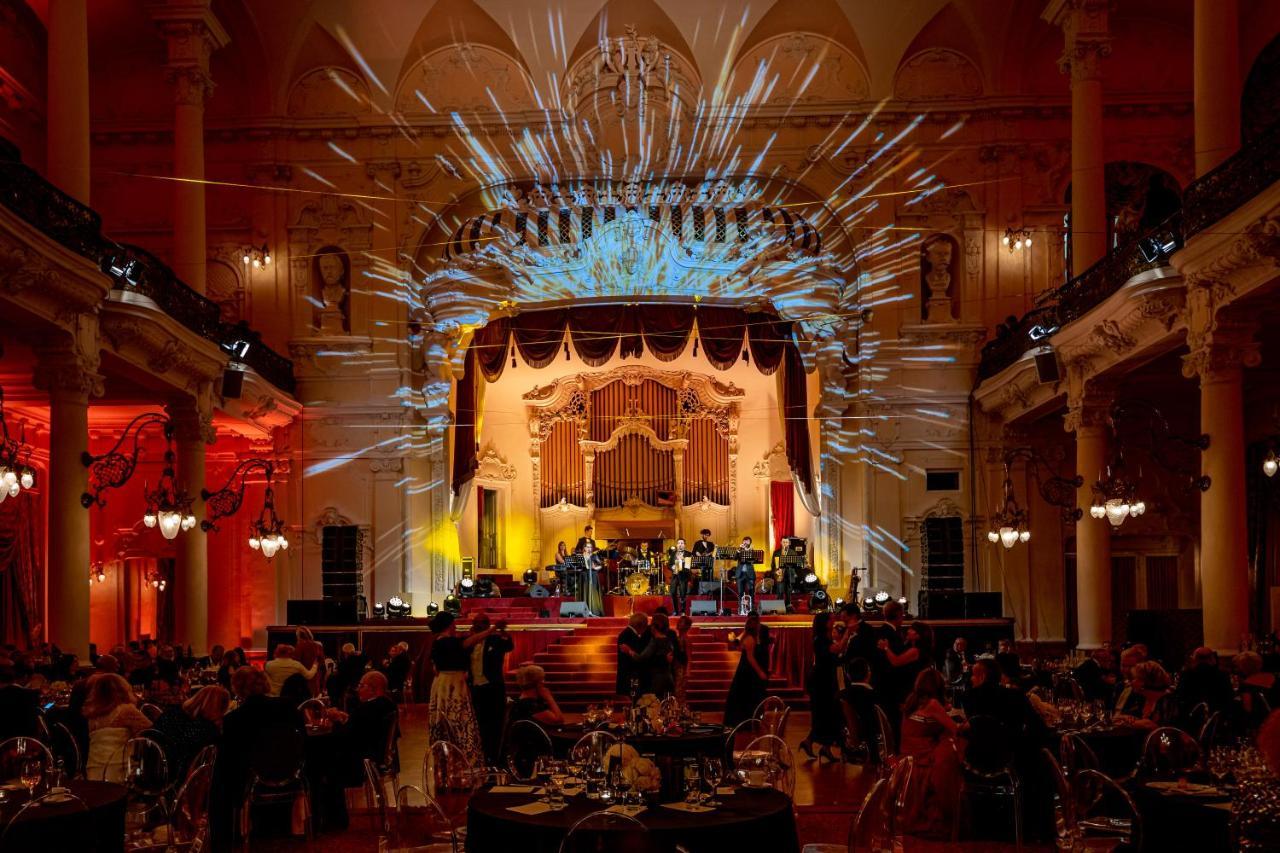 Grandhotel Pupp Κάρλοβι Βάρι Εξωτερικό φωτογραφία The photo depicts an elegant event taking place in a grand hall. The stage is beautifully decorated with ornate details, featuring colorful lighting and dramatic spotlights. A band or ensemble is performing on stage, while guests are seated at elegan