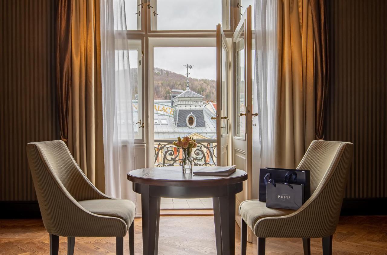 Grandhotel Pupp Κάρλοβι Βάρι Εξωτερικό φωτογραφία The photo depicts a cozy interior setting, likely within a hotel room or a private space. There are two elegant chairs positioned around a round wooden table. On the table, there is a small vase with flowers, adding a touch of warmth to the environme