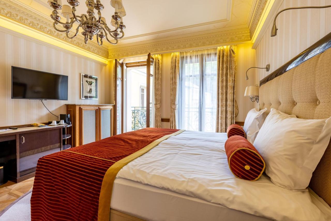 Grandhotel Pupp Κάρλοβι Βάρι Εξωτερικό φωτογραφία The photo shows an elegant bedroom designed with a warm and inviting ambiance. There is a large bed dressed in white linens and accented with a rich red bedspread. Two decorative pillows are placed at the head of the bed, adding to the room's sophist