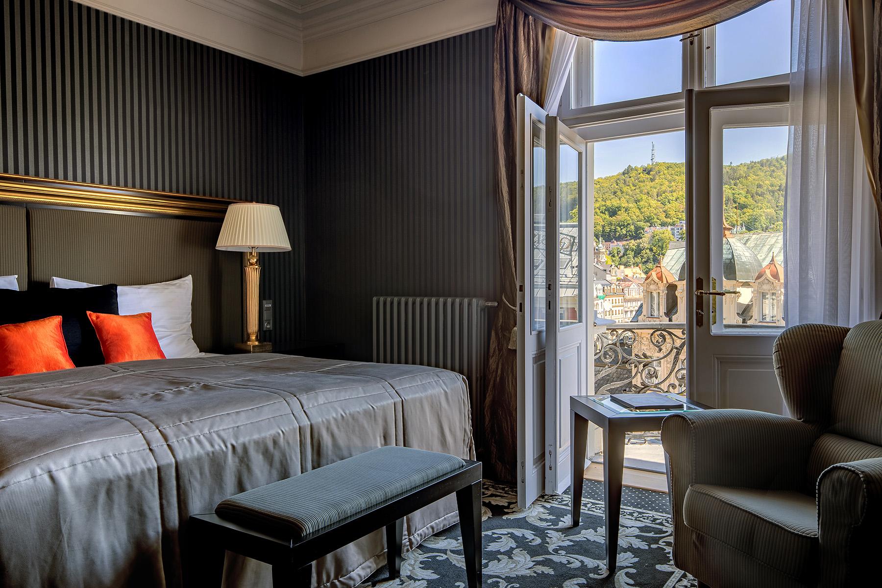 Grandhotel Pupp Κάρλοβι Βάρι Εξωτερικό φωτογραφία The photo shows a cozy hotel room with a sophisticated design. The room features a bed with a plush grey duvet and decorative pillows in black and orange. There is a bedside lamp beside the bed. A comfortable armchair sits in one corner. The room has
