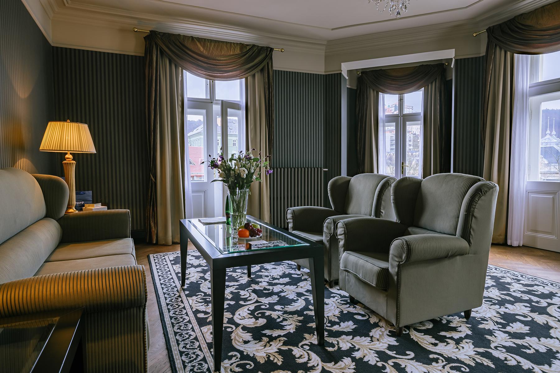 Grandhotel Pupp Κάρλοβι Βάρι Εξωτερικό φωτογραφία The photo shows a cozy living room with a warm and elegant decor. It features two green upholstered armchairs and a beige sofa. In the center, there’s a glass coffee table with a small vase of flowers. The room is enhanced by dark wallpaper and soft 