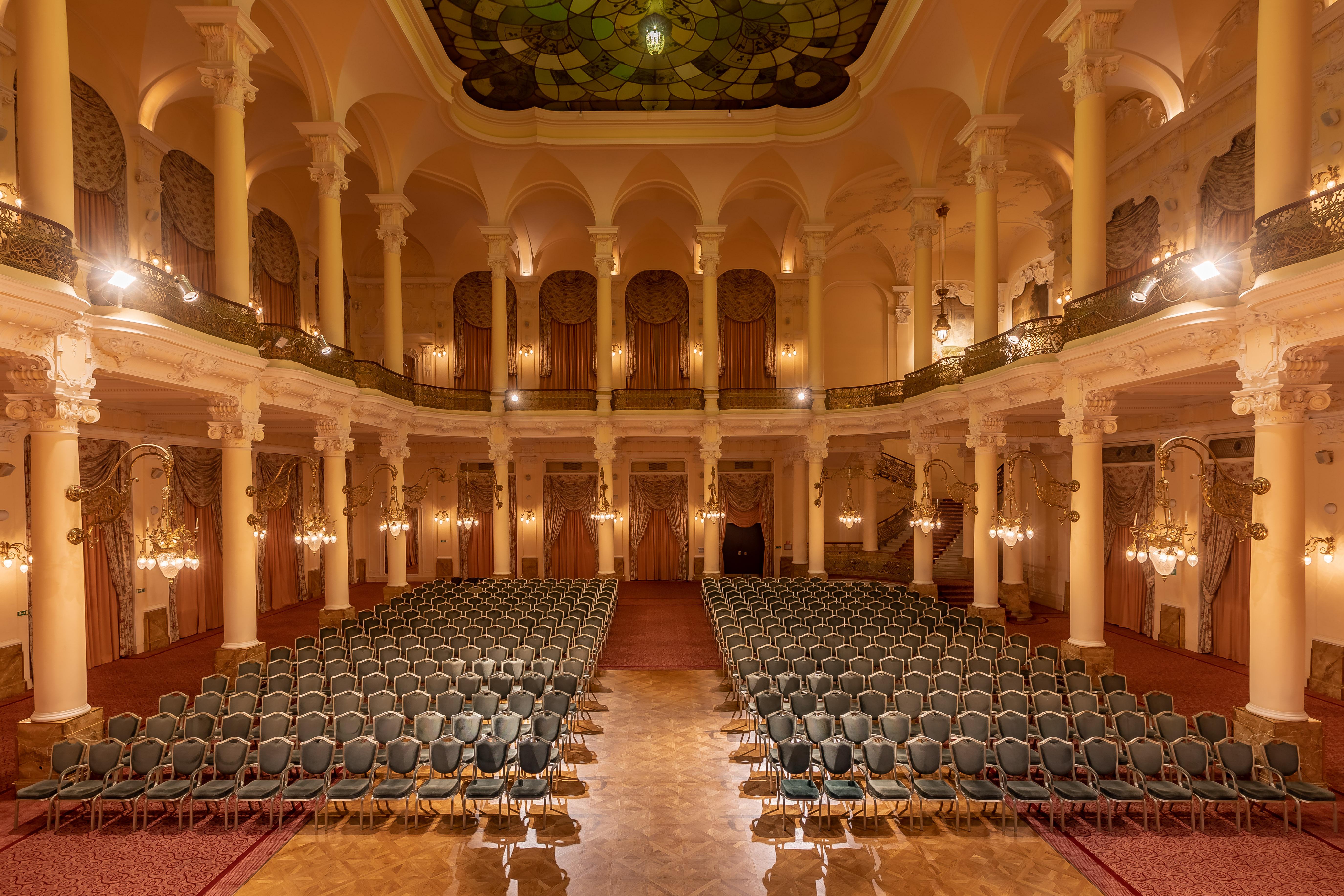 Grandhotel Pupp Κάρλοβι Βάρι Εξωτερικό φωτογραφία The photo shows an elegant, spacious auditorium or hall, designed for events or performances. The interior features high ceilings supported by tall, decorative columns. Rows of green upholstered chairs are neatly arranged, suggesting the space is set