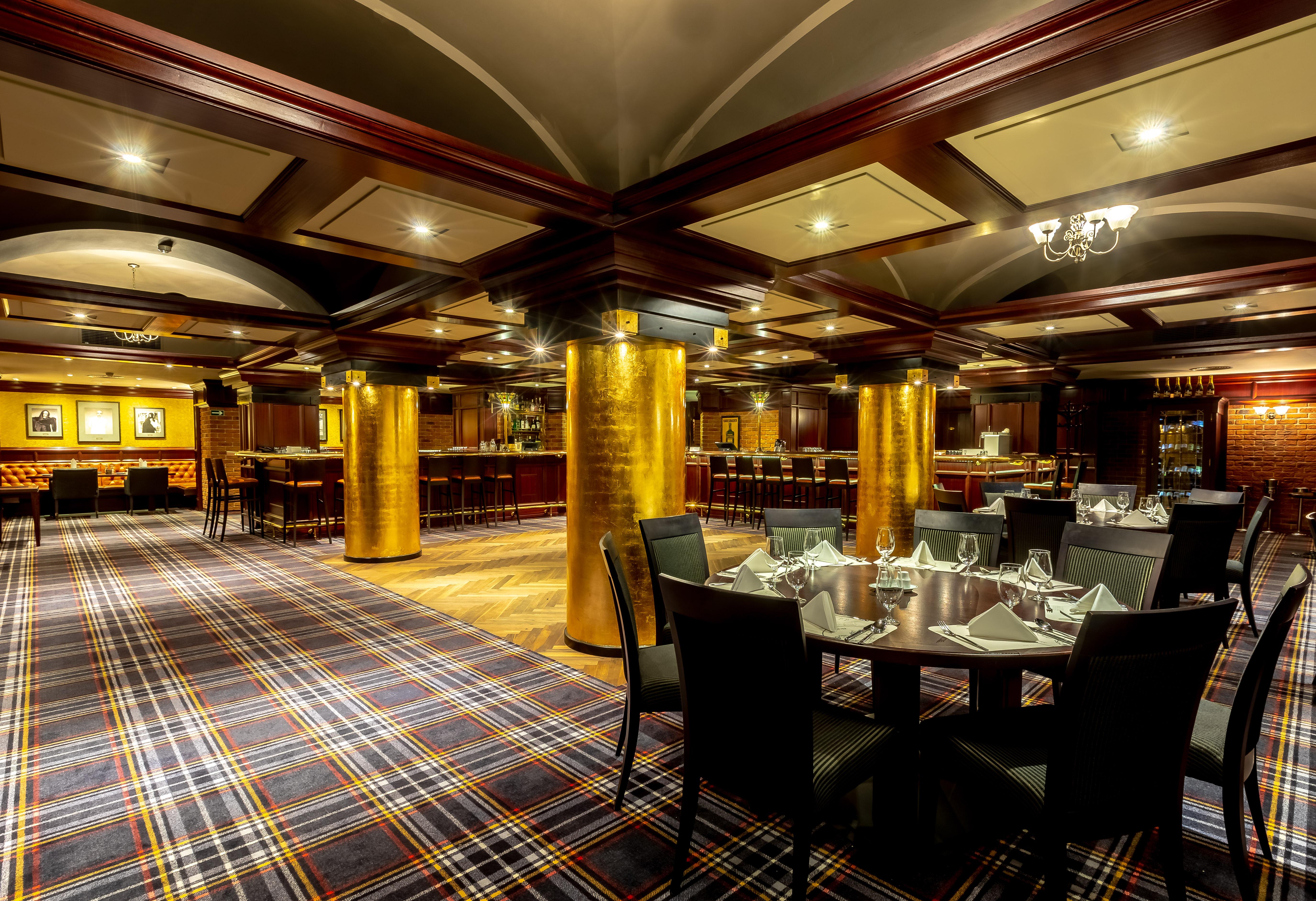 Grandhotel Pupp Κάρλοβι Βάρι Εξωτερικό φωτογραφία The photo shows an elegant dining area in a restaurant. The interior features a modern design with a checkered carpet and wooden accents. Golden columns are prominent in the space, adding a touch of luxury. The tables are set with neat tableware, and
