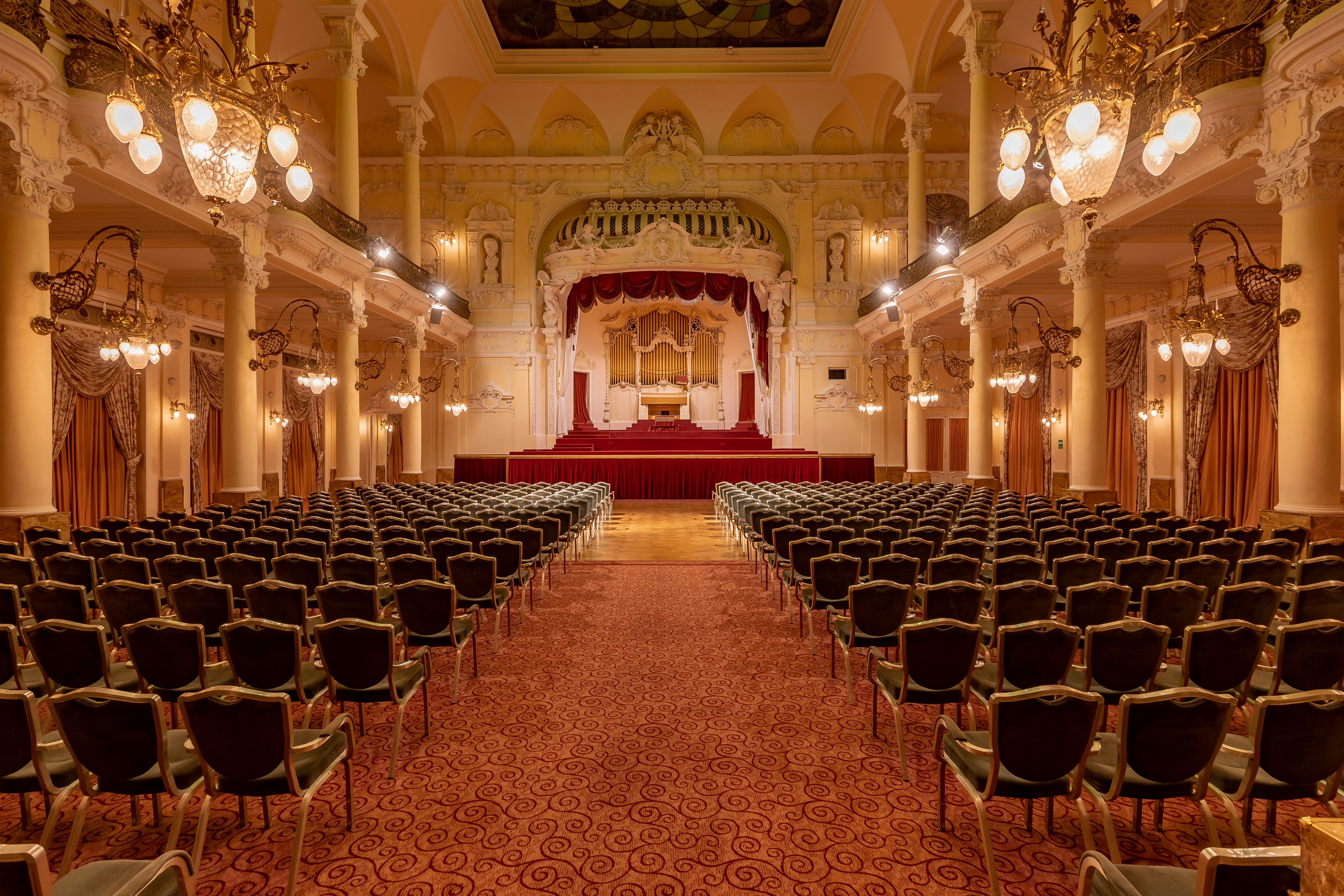 Grandhotel Pupp Κάρλοβι Βάρι Εξωτερικό φωτογραφία The photo showcases an elegant interior of a theater or concert hall. It features a grand stage in the background, adorned with red curtains and decorative elements. The seating area is filled with rows of green upholstered chairs arranged in a symme