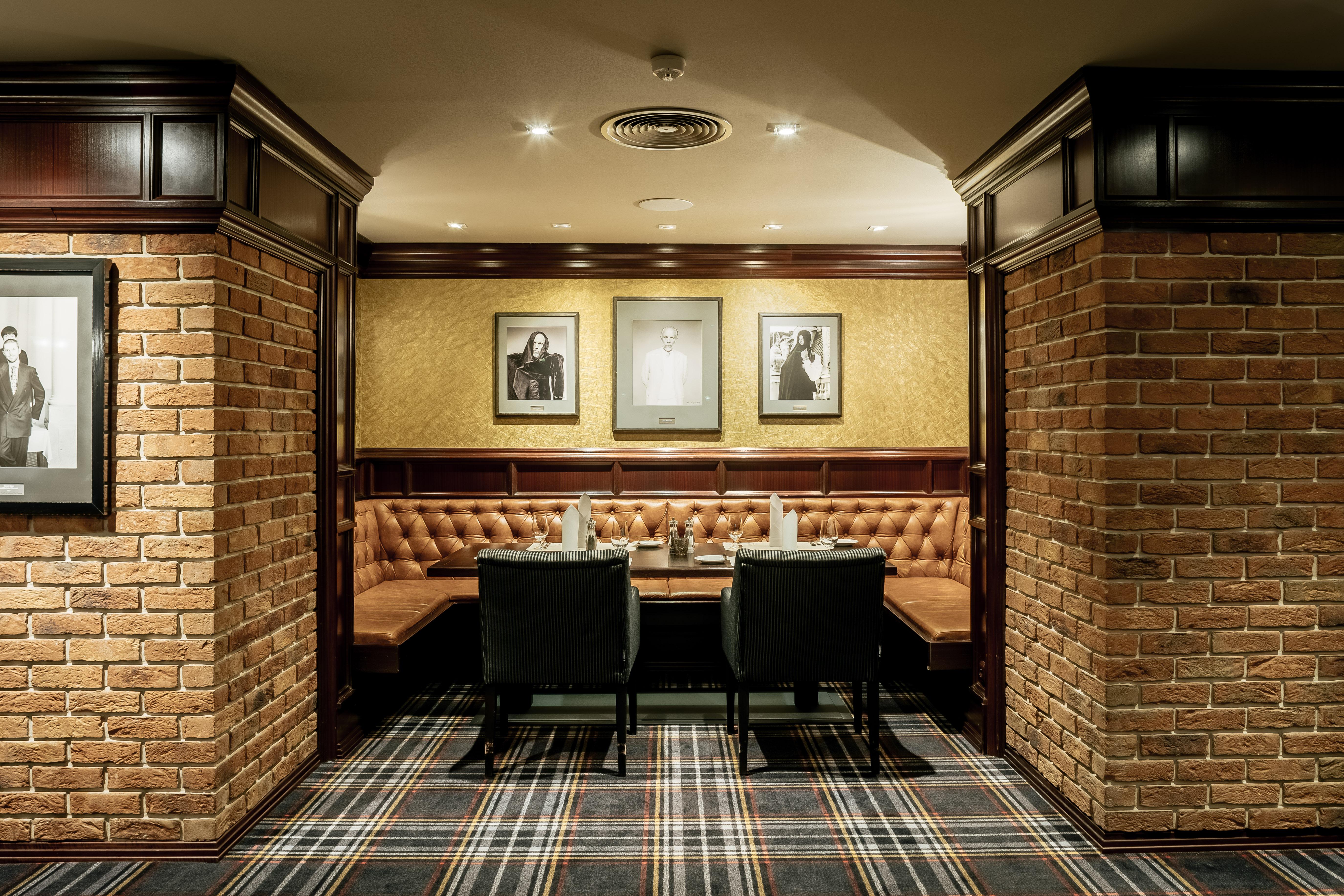 Grandhotel Pupp Κάρλοβι Βάρι Εξωτερικό φωτογραφία The photo depicts a cozy interior of a room, likely a restaurant or lounge. It features brick walls, giving it a rustic feel, and wooden paneling adds a touch of elegance. There are two black chairs positioned at a wooden table. The seating area is c