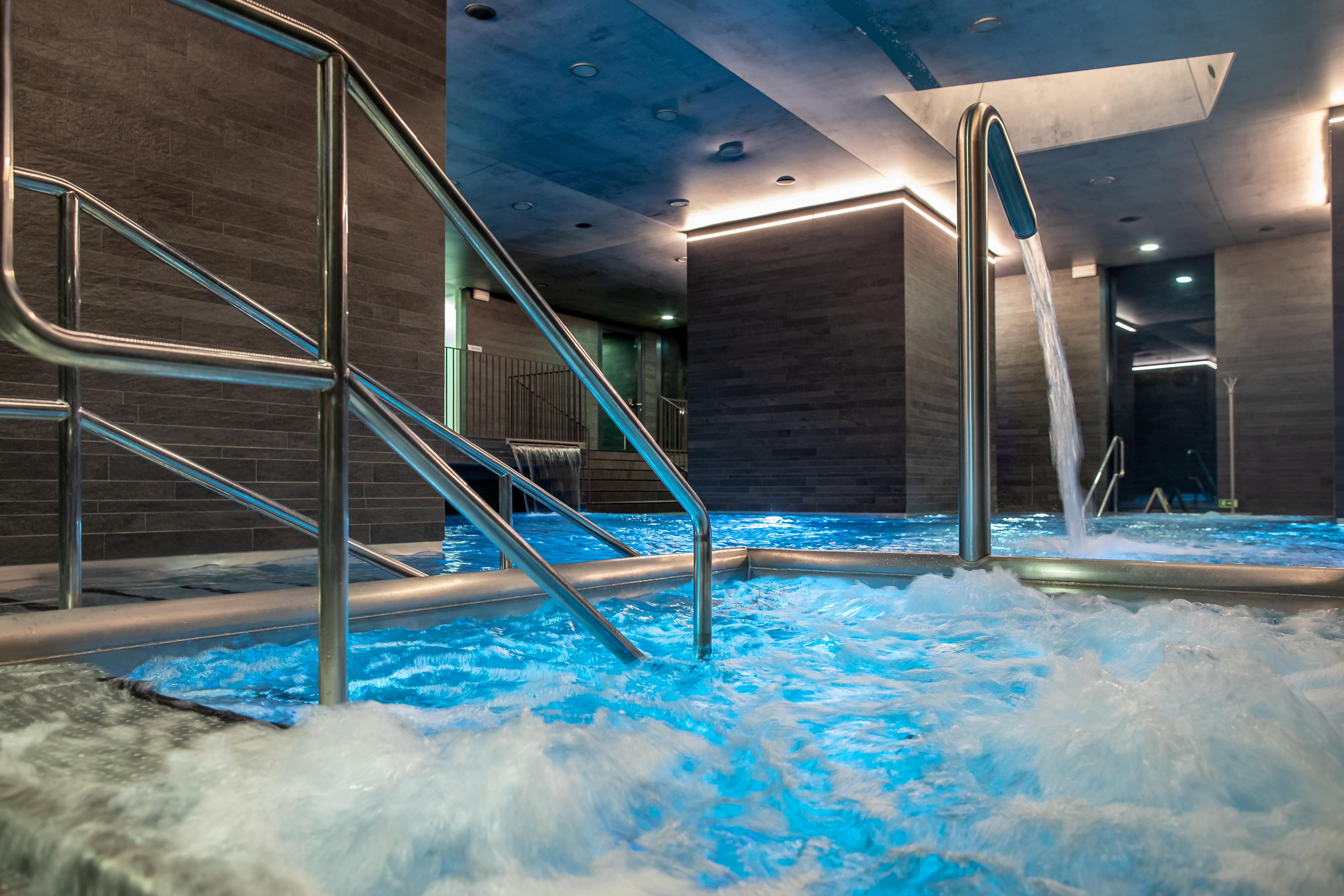 Grandhotel Pupp Κάρλοβι Βάρι Εξωτερικό φωτογραφία The photo shows a sleek, modern spa area featuring a hot tub or pool with bubbling, illuminated blue water. There are stainless steel handrails leading into the water. The walls have a contemporary design with a gray finish, and there are soft lights