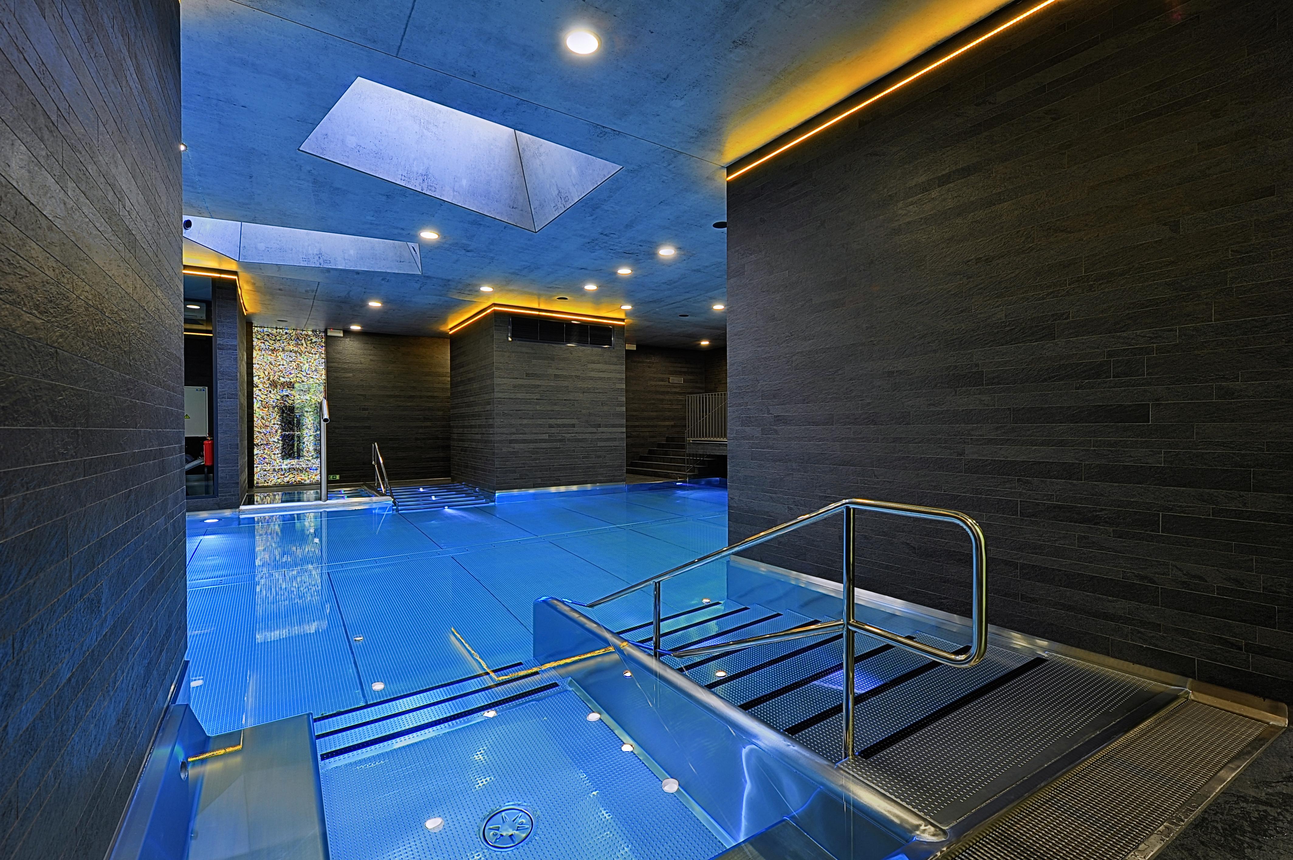 Grandhotel Pupp Κάρλοβι Βάρι Εξωτερικό φωτογραφία The photo features a modern indoor swimming pool area. The pool is designed with a sleek, contemporary aesthetic, featuring a vibrant blue water surface. The surrounding walls are made of dark materials, possibly stone or wood, complemented by warm l