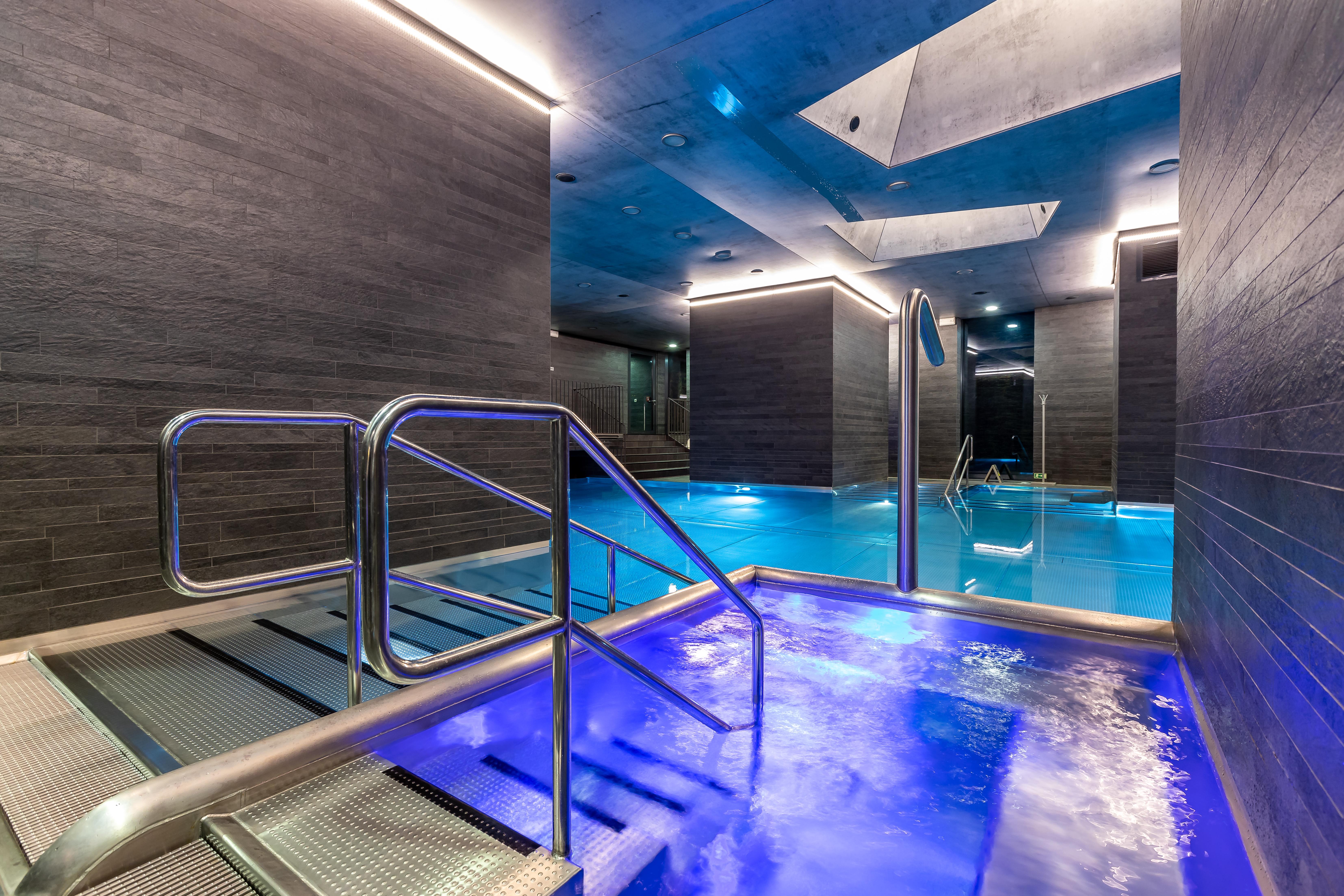 Grandhotel Pupp Κάρλοβι Βάρι Εξωτερικό φωτογραφία The photo shows a modern spa area with a pool. There are sleek, dark walls and blue lighting that creates a tranquil atmosphere. A metal railing leads down into the pool, which has a section with bubbling water. The overall design features clean line