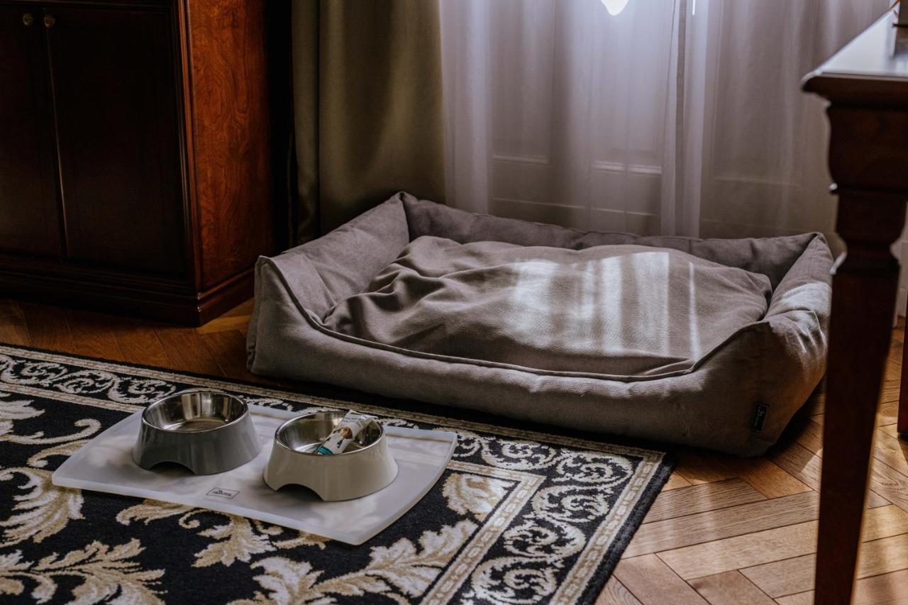 Grandhotel Pupp Κάρλοβι Βάρι Εξωτερικό φωτογραφία The photo shows a cozy pet area inside a room. There is a soft, rectangular pet bed in a muted color, positioned against a wall, with some light filtering through a window. In front of the bed, there are two pet bowls placed on a mat, one bowl is gre