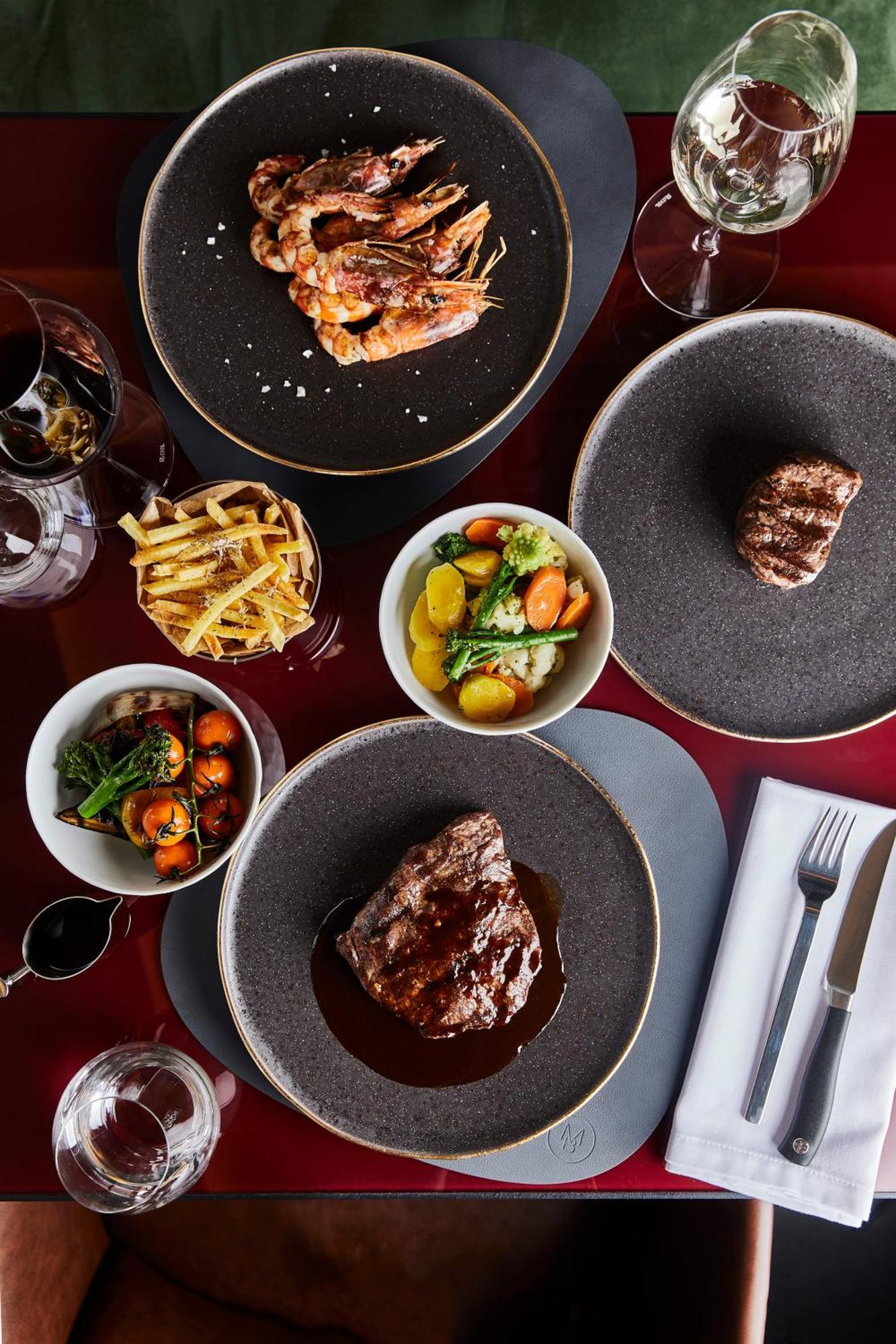 Grandhotel Pupp Κάρλοβι Βάρι Εξωτερικό φωτογραφία The photo features a gourmet meal spread across a dining table. Key elements include:

1. **Main Dishes**: There are two pieces of grilled steak, one prominently displayed at the bottom and another slightly obscured at the top right, both garnished w